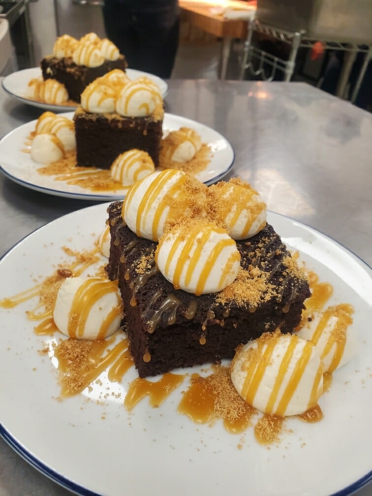 This image depicts a chocolate cake desert with whipped creme and a caramel drizzle.
